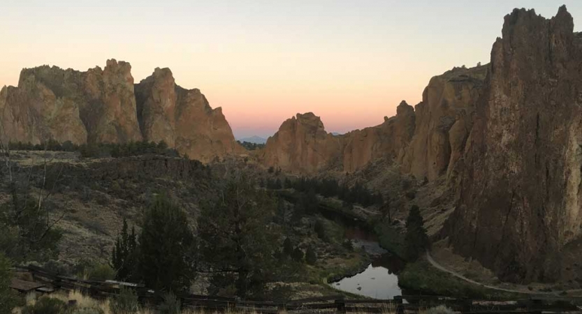 Large rock formations just upward amongst trees and a small body of water.